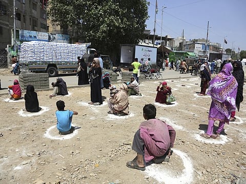 People sit at distance to receive relief goods during a nation-wide lockdown to contain outbreak of the coronavirus, in Karachi on Friday.