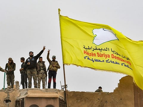 In this file photo taken on March 24, 2019 Fighters of the Syrian Democratic Forces (SDF) flash the victory sign next to their unfurled flag atop a roof at a position in the village of Baghouz in Syria.