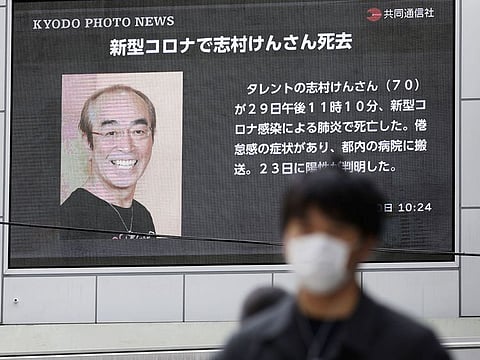 A man wearing a protective face mask, following an outbreak of the coronavirus disease (COVID-19), walks past in front of a huge screen reporting death of Japanese comedian Ken Shimura.
