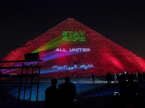 People take pictures of the Great Pyramid where a laser projection writes "Stay home, all united" on March 30, 2020, amid the spread of the COVID-19 infection, caused by the novel coronavirus.