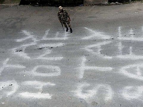 A police personnel stands guard over a message written on the road 'Stay Home Stay Safe' during complete lockdown amid coronavirus pandemic, in Jammu on Tuesday.