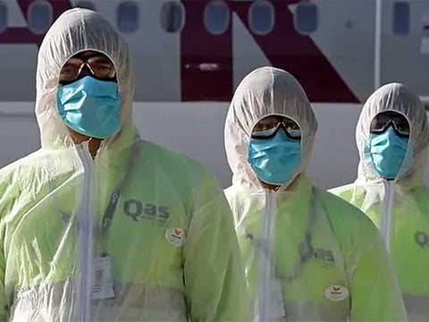 Employees of Qatar Aviation Services (QAS), wearing protective gear as a safety measure during the COVID-19 coronavirus pandemic, walk along the tarmac after sanitizing an aircraft at Hamad International Airport in the Qatari capital Doha on April 1, 2020. (AFP)