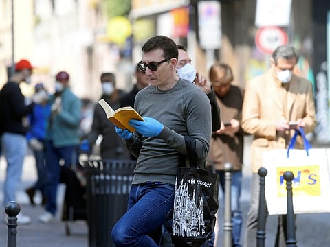 A man wearing protective gloves reads as he queues to a shop, as the spread of coronavirus disease (COVID-19) continues, in Milan, April 4.