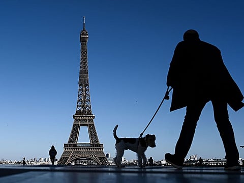A man walks his dog in front of the Eiffel Tower in Paris on April 5, 2020, on the 20th day of a lockdown in France aimed at curbing the spread of COVID-19