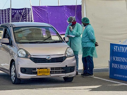 Medical staff members wearing protective gear take information from a resident sitting in a car for a coronavirus test at a drive-through screening and testing facility in Karachi.