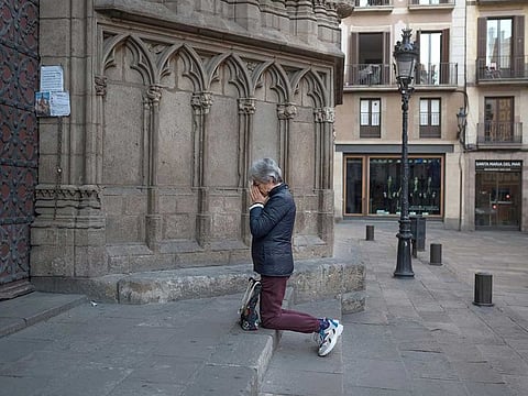A woman prays on her knees at the door of the Santa Maria Del Mar church in downtown Barcelona, Spain, Sunday, April 5, 2020