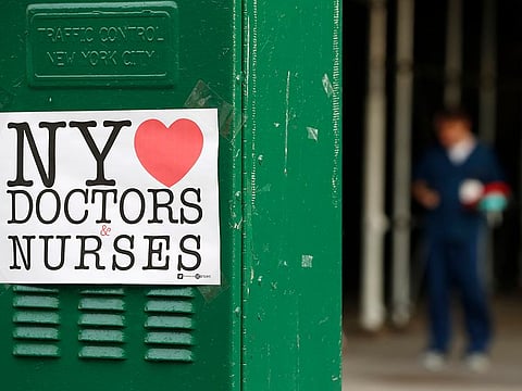 A sign acknowledging the work of doctors and nurses is posted on a traffic control box outside Brooklyn Hospital Center, as a hospital worker, right, waits for a traffic light to change before reporting to duty, Sunday, April 5, 2020, in New York.