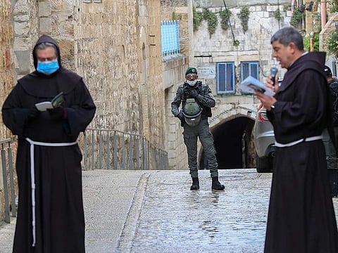 An Israeli soldier stands guard as Fransiscan friars pray at the first station while taking part in a small Procession of the Way of the Cross along the Via Dolorosa to mark Good Friday in Occupied Jerusalem, on April 10, 2020, amid the COVID-19 outbreak.