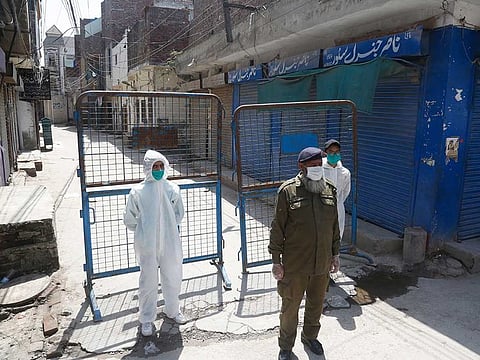 Pakistan volunteers and a police officer stand guard outside the area which authorities sealed after a group of people tested positive for the new coronavirus, Friday, April 10, 2020 in Lahore.