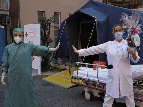 Monica Carfora, right, deputy head of the emergency of the Santo Spirito Hospital, which now has a separate emergency for possible covid patients, holds a chocolate Easter egg as she poses for a photograph with nurse Silvia Sforza, holding out their arms to indicating social distancing, outside the entrance to for COVID-19 emergency, in central Rome, Sunday.