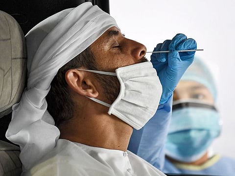 A medical staffer obtains a swab sample from a man inside a vehicle at a drive-through COVID-19 testing centre in Al Khawaneej, Dubai.