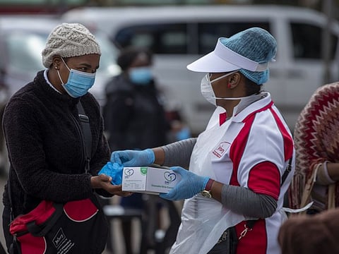 A health worker hands over surgical gloves to a woman, whilst queuing to undergo screening and testing for COVID-19, in Lenasia, south of Johannesburg, South Africa.