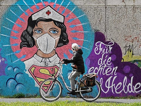 A cyclist ride past a coronavirus graffiti by street artist 'Uzey' showing a nurse as Superwoman in Hamm, Germany