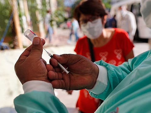A medical worker extracts a flu vaccine as an elderly woman waits to be vaccinated at the Ministry of Health in Asuncion, Paraguay, Tuesday, April 14, 2020. Health authorities are encouraging people over 60 to be vaccinated against the flu, also a respiratory disease, to reduce complications of those who might contact the new coronavirus.