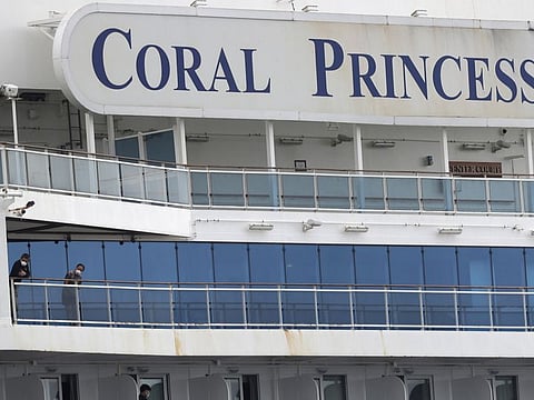 Passengers wearing protective masks look out from the Coral Princess cruise ship while docked at Port Miami during the coronavirus outbreak, Monday, April 6, 2020, in Miami. According to Princess Cruises, disembarkation of guests is expected to take several days due to limited flight availability. (AP Photo/Wilfredo Lee)