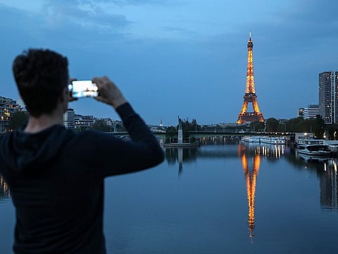 A man takes pictures of the Eiffel tower and its reflection on the Seine river, in Paris, on April 12, 2020, during the lockdown aimed at curbing the spread of the COVID-19 pandemic