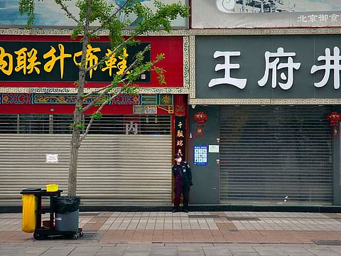 A security guard wears a facemask to protect against the spread of the new coronavirus as he stands next to shuttered shops at an outdoor shopping area in Beijing.