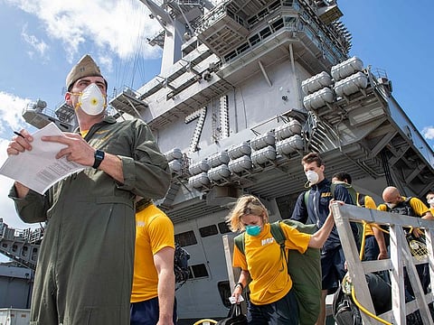 Sailors assigned to the aircraft carrier USS Theodore Roosevelt (CVN 71) wearing face masks as they depart the ship to move to off-ship berthing, April 10, 2020.