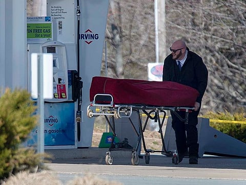 A worker with the medical examiner's office removes a body from a petrol station n Enfield, Nova Scotia, on Sunday, April 19, 2020.
