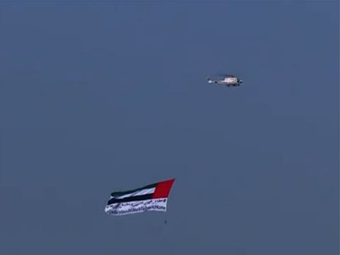 UAE flag with the message #DedicationatWorkandSafetyatHome flown over Abu Dhabi