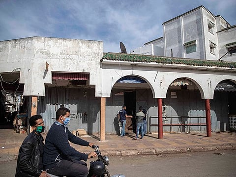 People wearing a face mask drive past empty shops during a health state of emergency and home confinement orders in Rabat, Morocco,
