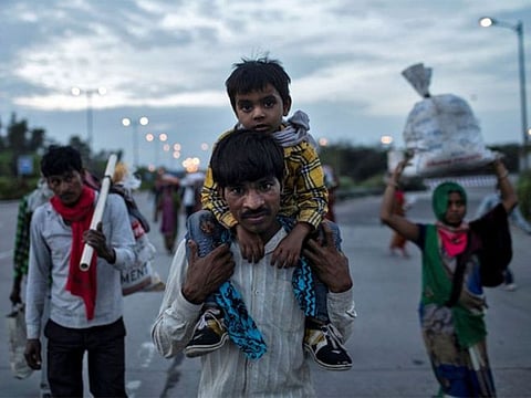 Indian migrant worker carries his son as they walk along a road with others to return to their village in New Delhi