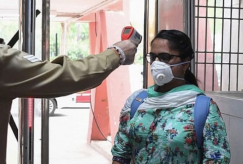 A cop checks the body temperature of a visitor in Delhi during a government-imposed nationwide lockdown as a preventive measure against the COVID-19 coronavirus