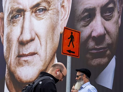 People walk past an election campaign billboard for the Blue and White party, the opposition party led by Benny Gantz, left, in Israel
