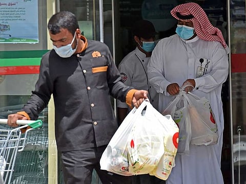 A worker and a man carry grocery bags during a nationwide curfew to stem the spread of COVID-19, as they leave a supermarket in the Saudi capital Riyadh on April 9, 2020 ahead of the fasting month of Ramadan.