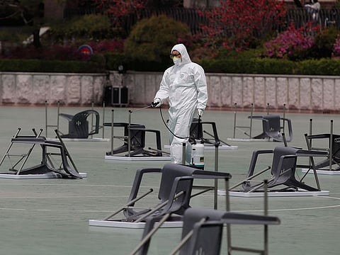 A worker wearing protective gears sprays disinfectant at desks and chairs before an insurance planner qualification exam in Seoul, South Korea, Saturday, April 25, 2020