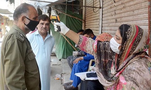 A health worker checks the body temperature of a policeman at Bibi Pak Daman Bazaar during a government-imposed nationwide lockdown.