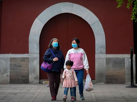 People wearing face masks to protect against the spread of the new coronavirus walk at a public park in Beijing, Saturday, April 25, 2020.