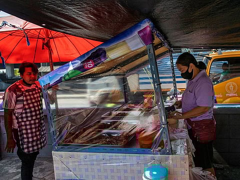 A street food vender standing behind plastic sheets to help curb the spread of the new coronavirus prepares a meal in Bangkok, Thailand, Tuesday, April 28, 2020.