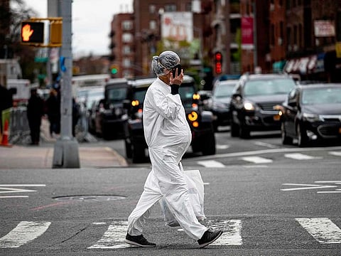 A pregnant woman wearing a hazmat suit and a mask walks in the street in the Elmhurst neighbourhood of Queens in New York City
