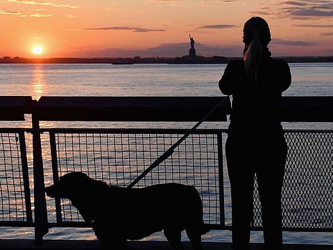 A woman walking her dog stops to look at the sunset over the Statue of Liberty amid the novel coronavirus pandemic on April 28, 2020 in New York City.