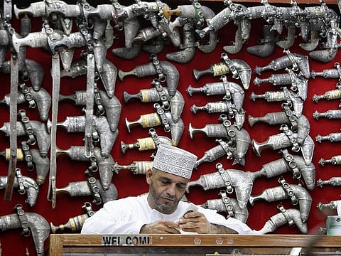 An Omani man sits in front of a display of jambiyas (traditional daggers) in Muttrah Souq, the oldest market in Oman, in the capital Muscat