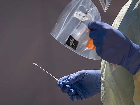 A medical personnel wearing personal protective equipment (PPE) holds a testing swab for COVID-19 at a drive-thru testing site.