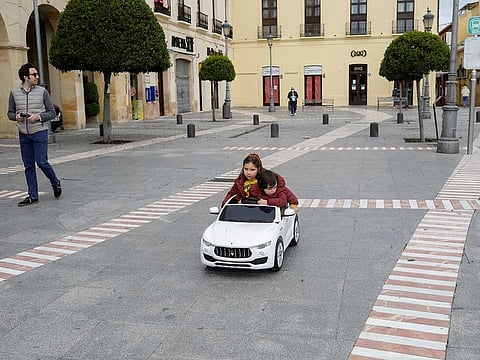 A man takes a walk with his children sitting in an electric toy car controlled by him at an empty square, after restrictions were partially lifted for children, during the coronavirus disease (COVID-19) outbreak in downtown Ronda, Spain, April 28, 2020.