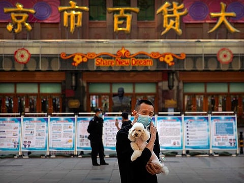 A man wearing a face mask to prevent the spread of the new coronavirus holds a dog as he stands along a pedestrian shopping street in Beijing, Tuesday, April 28, 2020. The Chinese city of Wuhan, which was the original epicentre of the pandemic, again reported no new coronavirus cases or deaths Tuesday and its hospitals remained empty of virus patients for a second straight day.