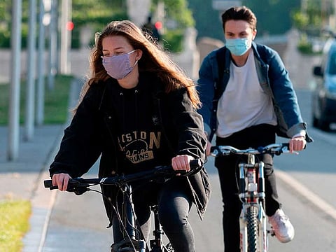 Students Lea Karner (L) and Dorian Di Giorgio arrive to the Akademisches Gymnasium high school on their bicycles on May 4, 2020 in Vienna on the day of the reopening of high schools in the country after more than a month of closure due to the new coronavirus pandemic.