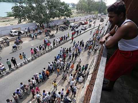 A man watches from his balcony as people stand in a queue outside a wine shop after authorities allowed the sale of liquor with certain restrictions, during the ongoing COVID-19 nationwide lockdown, in New Delhi on Monday.