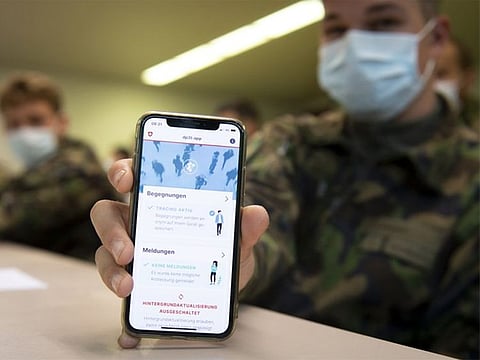 A soldier of the Swiss army wearing a protective face mask holds a smartphone with an app using Decentralized Privacy-Preserving Proximity Tracing (DP-3T) during a test with 100 soldiers in the military compound of Chamblon near Yverdon-les-Bains, Switzerland.