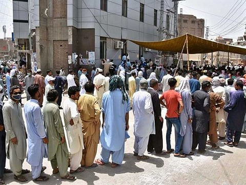 A large number of people wait in front of a bank in Sindh province without taking proper precautionary measures such as social distancing to prevent the spread of COVID-19.