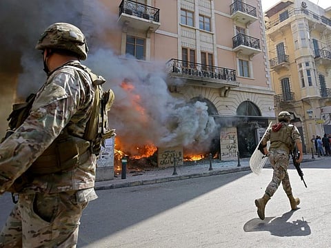 Lebanese soldiers clear the road next to a burning bank branch, set ablaze by demonstrators in the northern port city of Tripoli on April 28.