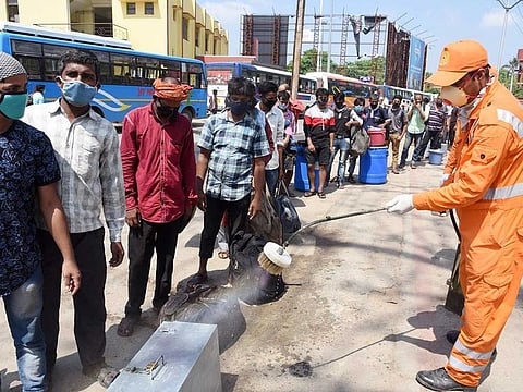 Workers disinfect the luggage of migrants as they stand in a queue to board a bus to go back home, in Patna.