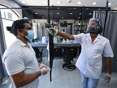 A hairdresser checks a colleague's temperature as they resume work at a salon in Dubai Marina.