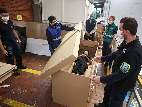 Rodolfo Gomez, to centre, and his employees demonstrate how their design of a cardboard box can serve as both a hospital bed and a coffin, designed for COVID-19 patients, in Bogota, Colombia.