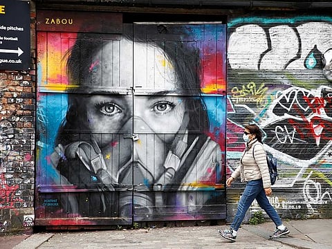 A woman wearing a protective face mask walks past streetart in Shoreditch, London.