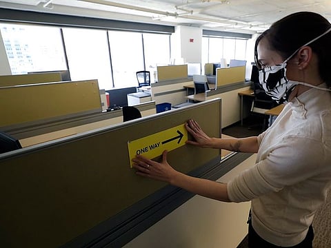 Interior Designer Stephanie Jones at the design firm Bergmeyer putting up a safe distancing reminder indicating one way foot traffic to a cubicle at the firms offices in Boston. When workers around the world eventually return to their desks, they’ll find myriad adjustments by their companies to reflect the post-pandemic “new normal” way of life, executives and experts say.