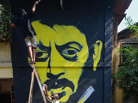 A girl cycles past as Indian artist Ranjit Dahiya (C) instructs a colleague while working on a wall mural of Bollywood actor Irrfan Khan in Mumbai on May 1, 2020. Acclaimed Indian actor Irrfan Khan, whose international movie career included hits such as "Slumdog Millionaire", "Life of Pi" and "The Amazing Spider-Man", has died aged 53, his publicist said on April 29. / AFP / INDRANIL MUKHERJEE